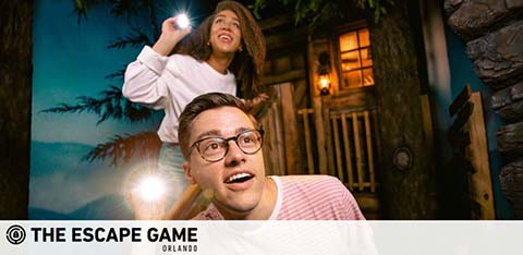 Two people looking excited at an escape room game with a flashlight and themed backdrop.