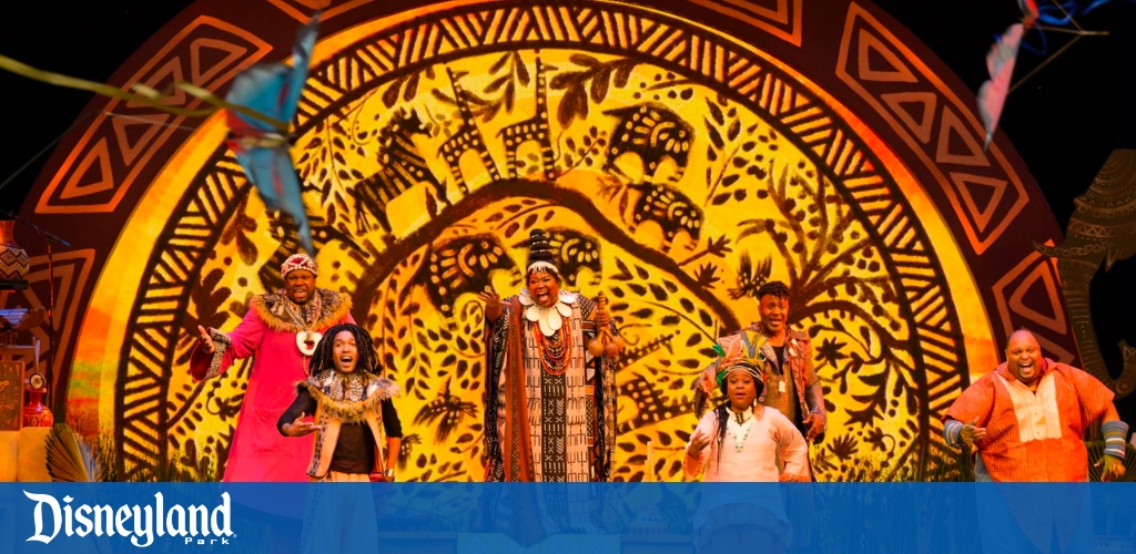 Performers in vibrant attire on stage with a cultural backdrop at Disneyland Park.