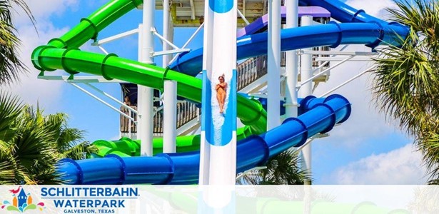 The image shows a vibrant scene at Schlitterbahn Waterpark in Galveston, Texas, with a person sliding down an intertwining blue and green water slide amidst lush palm trees against a clear blue sky.