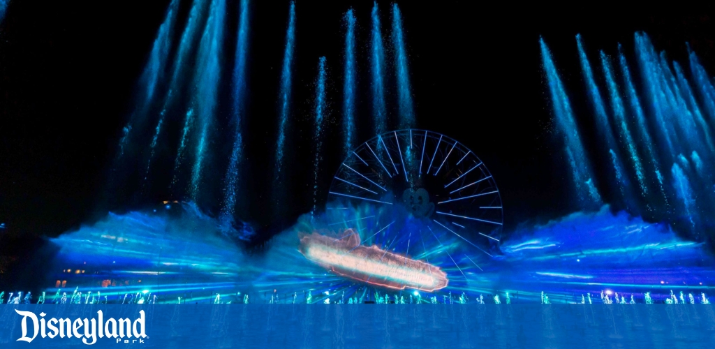 Nighttime water show with illuminated fountain jets and a Ferris wheel. "Disneyland Park" logo visible.