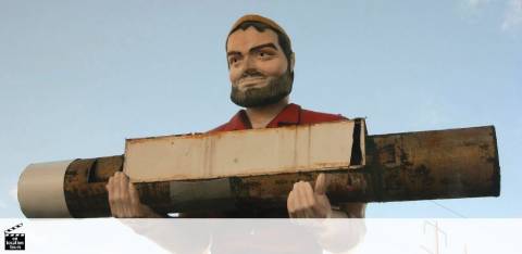 A large figure of a smiling man with a beard is depicted carrying an oversized pencil on his shoulder against a clear sky. The pencil and the man’s posture resemble a worker carrying lumber, reflecting a playful take on physical labor.