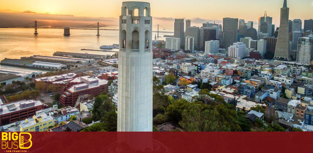 Image Description: This is an aerial photograph taken at dusk showcasing a panoramic view of an iconic cityscape. To the left, one can observe a large suspension bridge spanning across a body of water towards a hazy horizon where the sun is setting. The bridge's towers are partially silhouetted against the orange-tinted sky. In the foreground on the right, a prominent historic white tower stands tall, with its intricate design and arched windows noticeably distinguishing it from the surrounding architecture. The tower is positioned closely to the camera, making it a central feature of the image. Moving towards the center and further into the background, the dense urban landscape unfolds with an array of buildings varying in height, shape, and color. Numerous skyscrapers dominate the city's skyline, with one notably pointed building towering above the others. The buildings are illuminated by the soft, fading daylight which bestows a warm glow across the rooftops and facades, enhancing the visual depth of the scene. The image conveys the essence of a bustling, vibrant city winding down as the day transitions into evening.

End Sentence: At FunEx.com, we're committed to offering the lowest prices and biggest savings on tickets to explore magnificent cities like the one featured in this image.