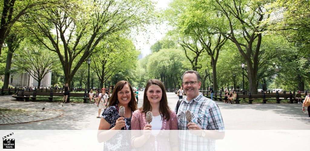 Three people are standing in a sunny park with green trees. They’re smiling and holding ice cream cones. The background features park benches and strolling pedestrians. A watermark in the bottom left corner reads  On Location Tours. 