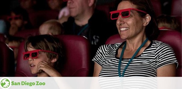 Audience members enjoy a 3D movie at San Diego Zoo. A smiling woman in a striped top and a boy wearing red 3D glasses are prominently featured, reflecting the fun and educational experience offered by the zoo's cinema.