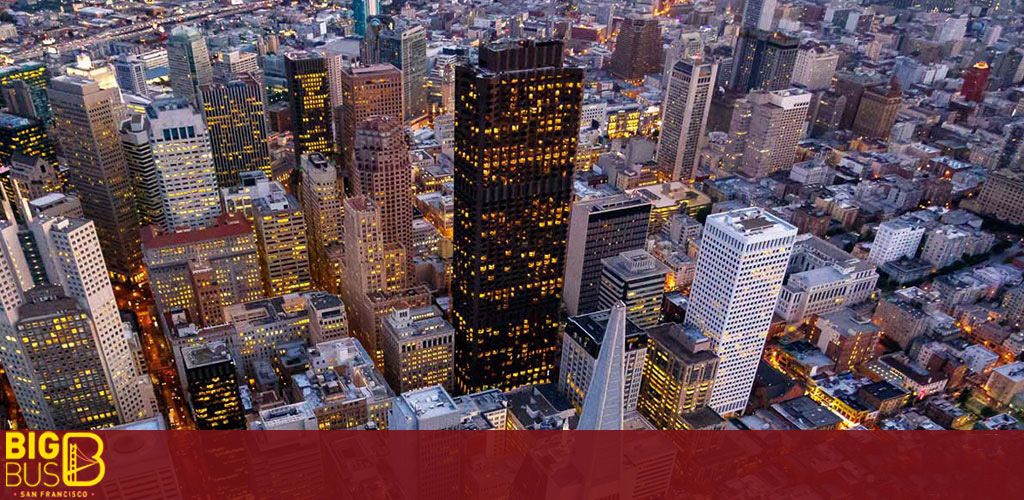 This image offers a breathtaking aerial view of a bustling metropolitan area during dusk. The cityscape is densely packed with skyscrapers of varying heights, many illuminating with interior lights against the twilight sky. Architectural details include modern glass-faced buildings along with more traditional structures with exterior lighting accentuating their facades. The streets below are not visible, suggesting a high vantage point. The variation in building size and design conveys the dynamic character of an urban center. In the bottom left corner, there is a watermark logo reading "BIG BUS SAN FRANCISCO." 

For an unforgettable experience exploring this vibrant cityscape, book a city tour with FunEx.com, where you can always find the lowest prices and great savings on tickets.