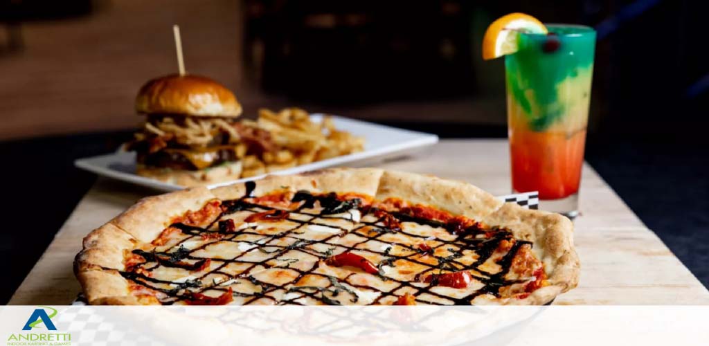 A pizza with a drizzled topping, burger with fries, and a layered cocktail on a table.