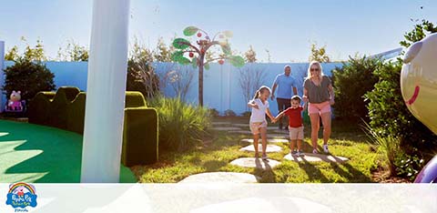 Family with two kids walking in a sunlit outdoor area with playful decorations.