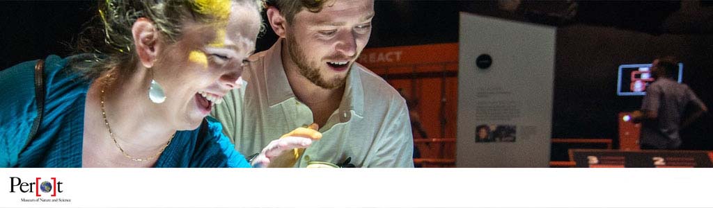 Banner image featuring a smiling woman with face paint and a man looking at a bright display inside the Perot Museum of Nature and Science. Exhibit information is visible in the softly focused background. The museum's logo is at the bottom left.