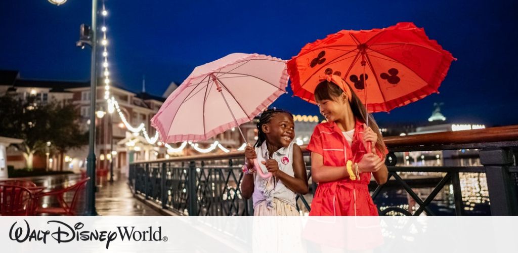 Two children are joyfully walking on a bridge at night, each holding a colorful umbrella. One wears a pink outfit with a pink umbrella, the other wears red with a red umbrella adorned with black Mickey Mouse shapes. The background features festival lights and a waterfront, creating a magical atmosphere. Perfect for a fun-filled Disney adventure.