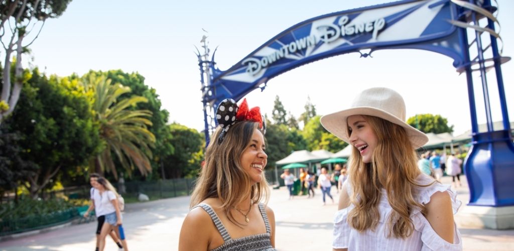 Two friends smiling in front of the Downtown Disney District entrance at Disneyland Resort.
