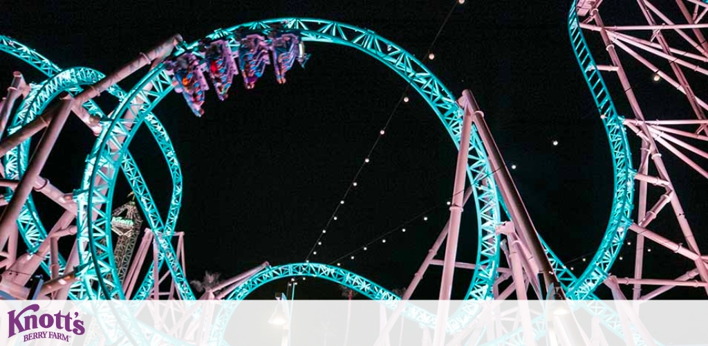 Image displaying a roller coaster at Knotts Berry Farm during nighttime. Blue tracks create intricate loops against the dark sky as a train filled with riders hangs upside down at the crest of a loop. The coaster's support structures crisscross around it, accentuating the thrill of the ride.