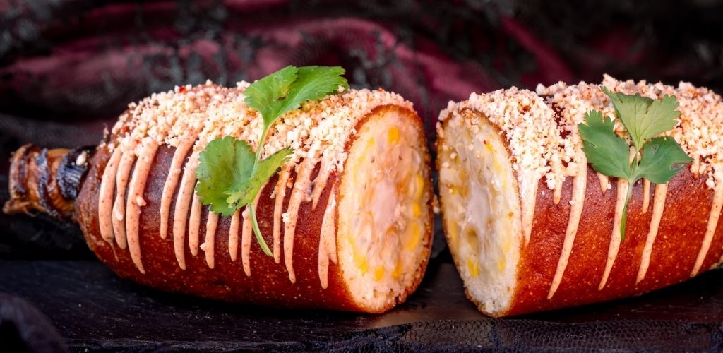 A roasted stuffed chicken breast covered with pink drizzle and breadcrumbs, garnished with fresh cilantro leaves on a black surface.