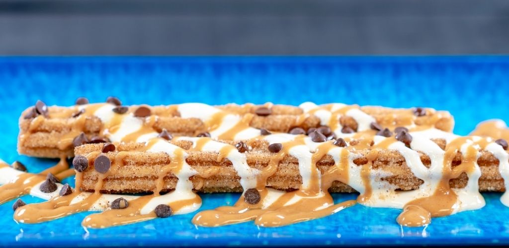 Chocolate chip cookie bar topped with caramel and white drizzle on a blue surface