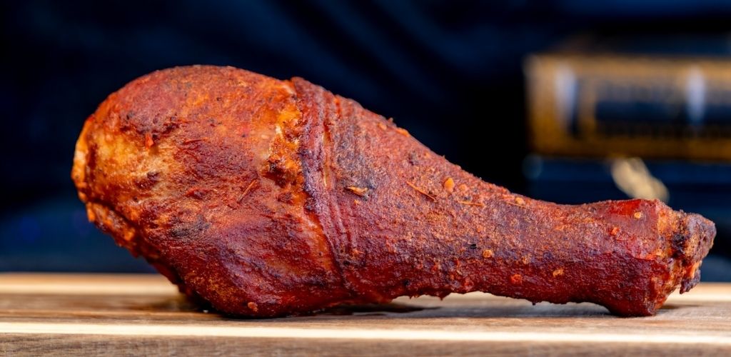 A cooked chicken drumstick with crispy skin placed on a wooden surface.