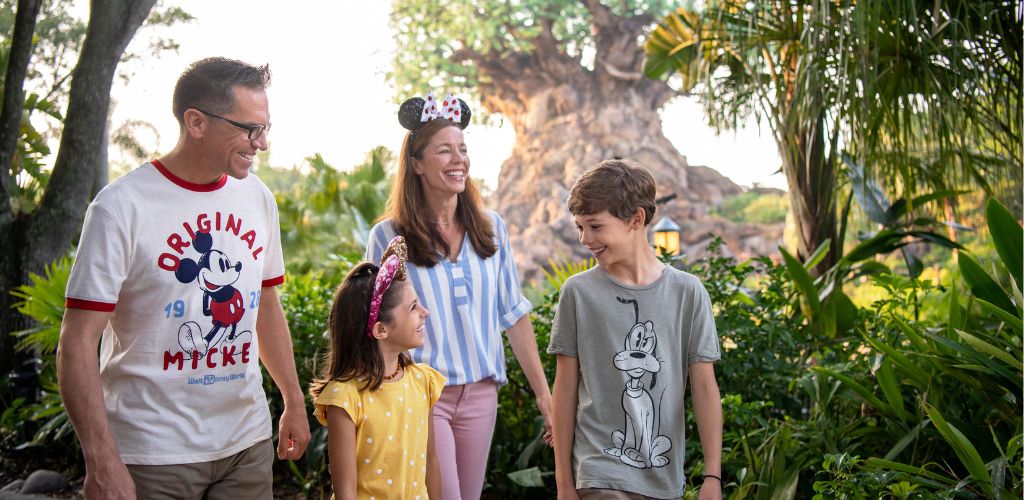 A family of four walking outdoors in a lush garden with trees and greenery, smiling and enjoying each other's company.