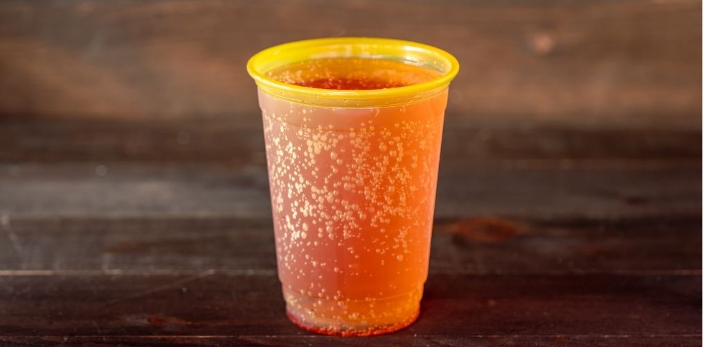 A clear plastic cup filled with reddish orange carbonated soda on a wooden surface.