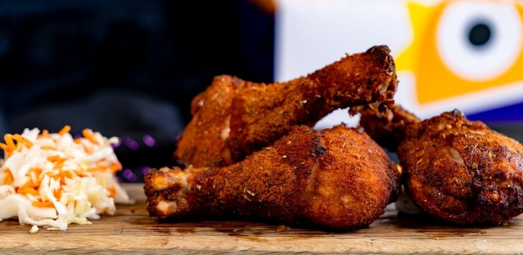 Three pieces of crispy fried chicken drumsticks and thighs with coleslaw on a wooden surface