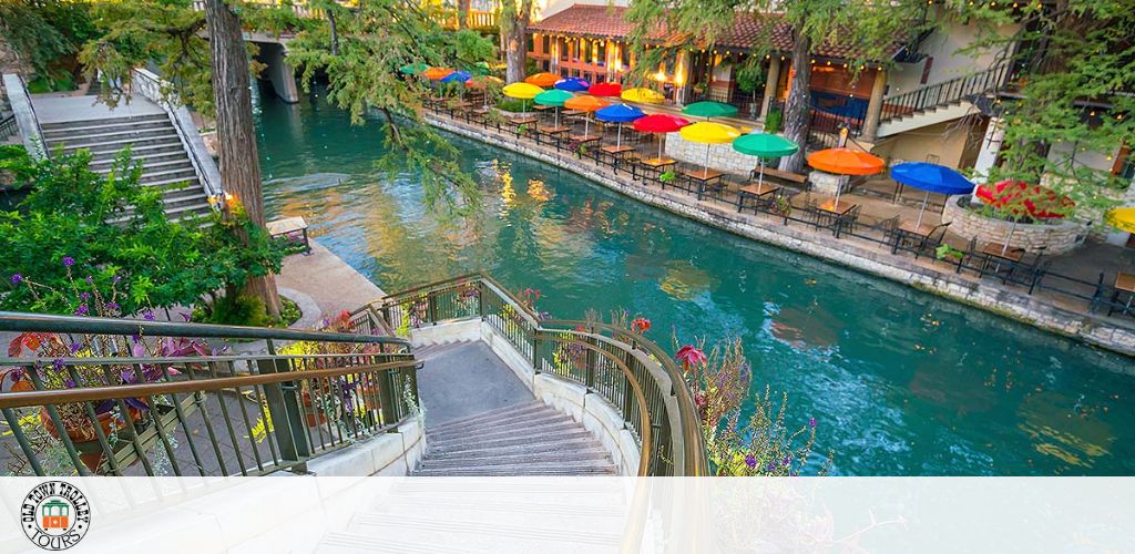 View of a riverwalk with colorful umbrellas, railings, and greenery.