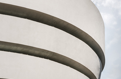 A top-down view of a museum with a distinctive spiral layout. Visitors dot the open floors and centralized courtyard. The design creates concentric off-white rings, each level featuring a balcony that overlooks the central space.