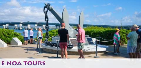 Image shows a group of people visiting an outdoor exhibit with a large anchor and propeller on display. Bright sky and greenery in the background. Text overlay at the bottom reads 'E NOA TOURS'.