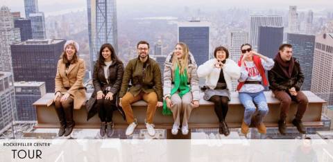 Image of seven individuals seated on a ledge at the Rockefeller Center tour, with a panoramic view of skyscrapers behind them. They are casually dressed, smiling, and appear to be enjoying their outing. The city skyline stretches into the distance under a cloudy sky. Text 'ROCKEFELLER CENTER TOUR' is visible at the bottom.