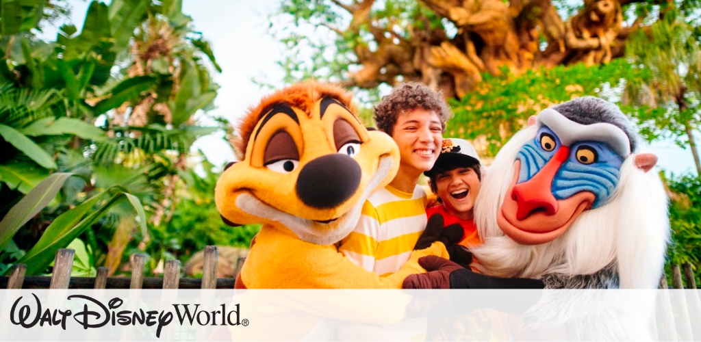 Two people pose joyfully with costumed characters Timon and Rafiki from The Lion King in a lush green setting at Walt Disney World. They are smiling and appear to be having fun outdoors, with trees and foliage in the background. The scene conveys a cheerful, family-friendly atmosphere.