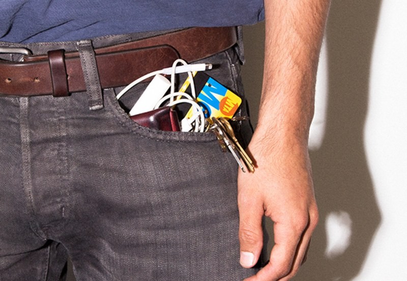 Man's pockets overflow with personal belongings. Metro card, keys, earphones and more.