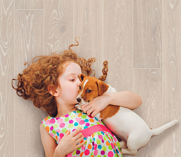 A pretty young girl nuzzles with her adorable puppy on a Kahrs floor