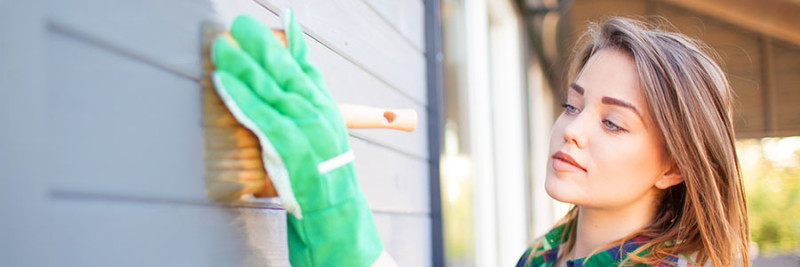 A young woman is painting the exterior of her home