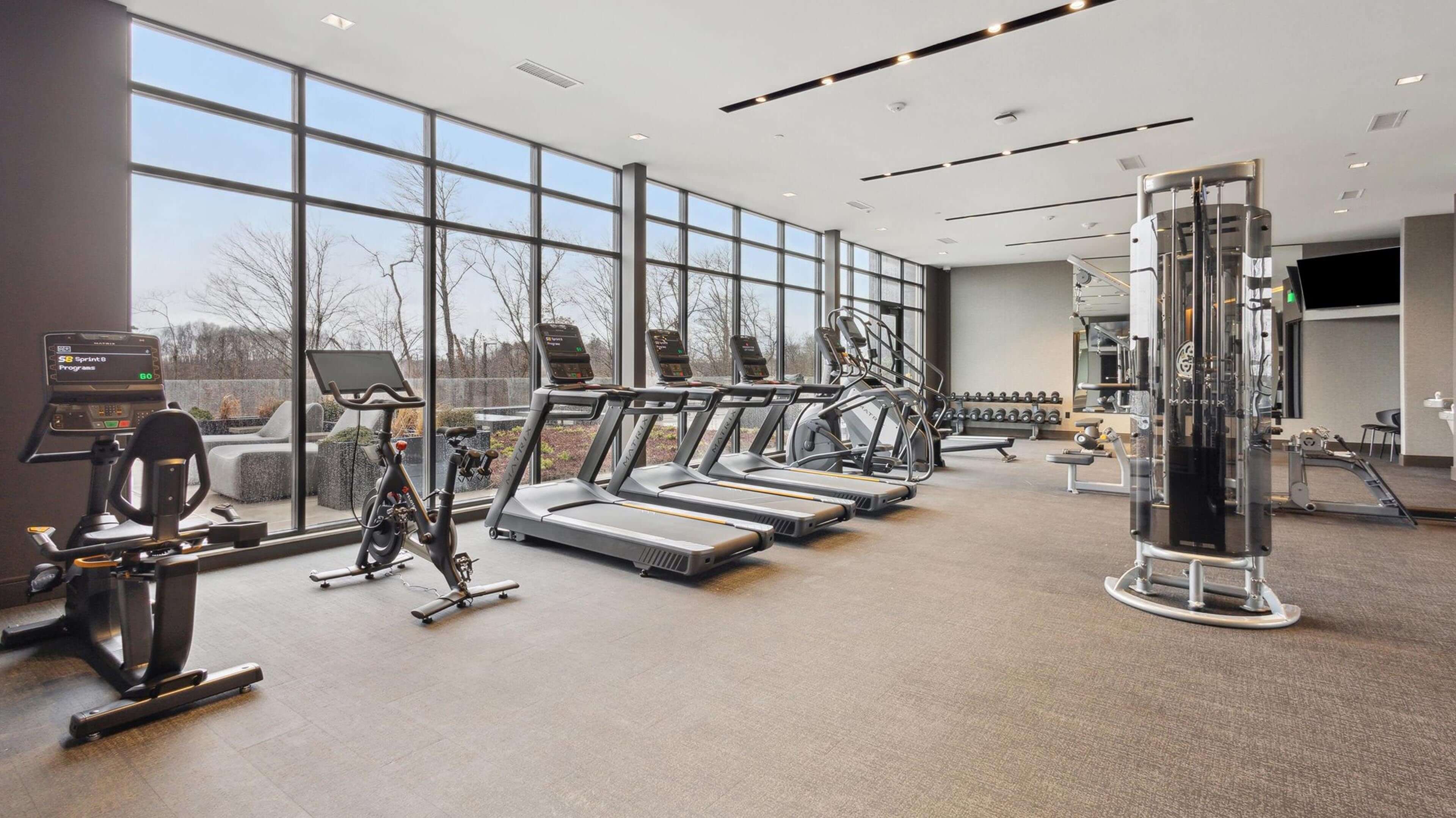 3D rendering of workout area in use by residents with large windows showing greenspire outside.