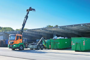 Symbolbild: Lkw mit grünen Containern vor einer Halle