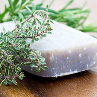 Handgemachte Naturseifen-Stücke mit Oregano und Rosmarin auf einem Holzbrett