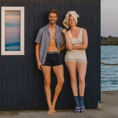 Frau und Mann in natürlicher Bio-Unterwäsche aus Bio-Baumwolle vor einer Badehütte am See.