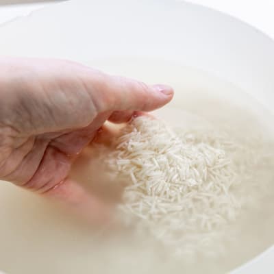Eine Frau wäscht weißen Reis in einer Schüssel mit Wasser. Hochwertiges Foto