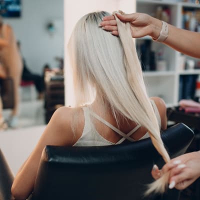  Eine Friseurin bringt einer jungen Frau mit blondem Haar in einem Schönheitssalon Haarverlängerungen an.