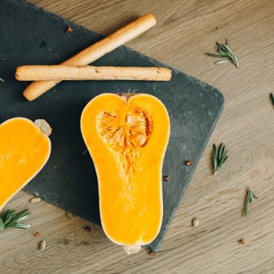 Vogelperspektive auf geschnittenen Butternut-Kürbis mit Kräutern und Brotstangen auf einem Schieferbrett.