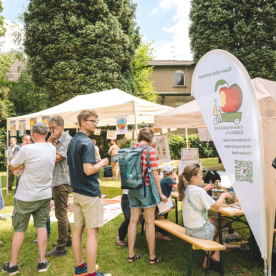Besucher*innen am Stand des Ernährungsrats Essen auf dem Gutes Klima Festival, Kinder experimentieren an einer Bierbank, Pavillons auf der Wiese.