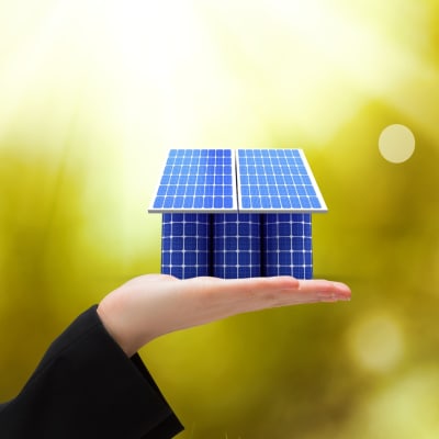 Ein haus aus Solarpaneelen  platziert auf einer Hand.