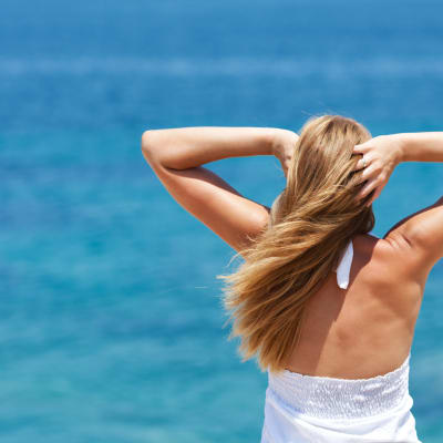 Junge schöne Frau mit den Händen im Haar, die sich entspannt und aufs Meer schaut