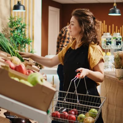 Ein fleißiger, umweltbewusster Mitarbeiter eines Lebensmittelladens füllt die Regale mit frischem Obst und Gemüse auf. Der Inhaber eines Supermarkts in der Nachbarschaft legt Lebensmittel aus biologischem Anbau in die Auslage.