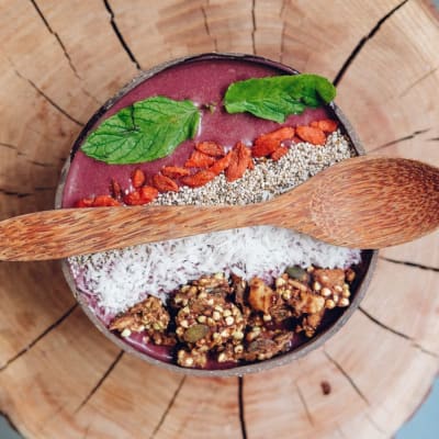 Gesunde Açaí-Schüssel mit Granola, Minzblättern und Beeren, serviert auf rustikalem Holz.