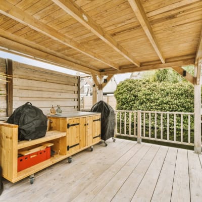 Ein Außenküchenbereich mit Holzboden und großen Topfpflanzen an der Seite der Terrasse mit Blick auf den Hinterhof.
