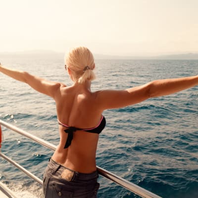 Rückansicht einer schönen jungen Frau, die mit erhobenen Armen eine Kreuzfahrt genießt.