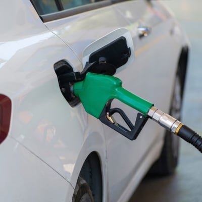 Nahaufnahme eines grünen Zapfhahns, der ein weißes Auto an einer Tankstelle betankt.