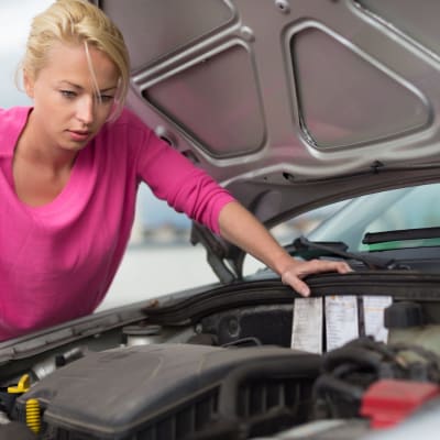 Eine moderne junge Frau untersucht einen defekten Automotor
