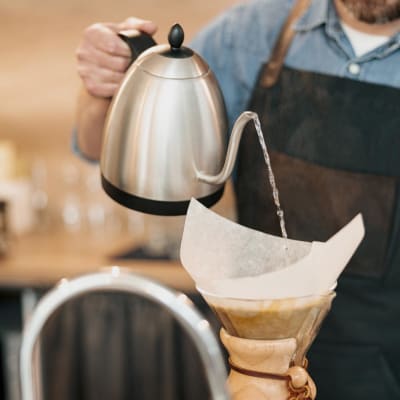 Barista mit einem Wasserkocher in der Hand, der kochendes Wasser durch einen Filter in eine Tasse gießt