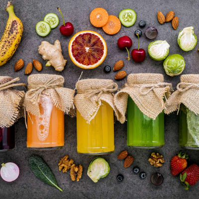 Farbenfrohe, gesunde Smoothies und Säfte in Flaschen mit frischen tropischen Früchten und Superfoods vor einem dunklen Stein-Hintergrund mit Platz für Text.