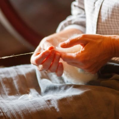 Die Hände einer Person, die Wolle mit traditionellen Methoden zu Garn spinnt.
