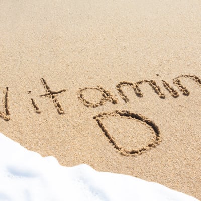 Vitamin D, geschrieben im Sand mit dem Schaum einer heranrollenden Welle