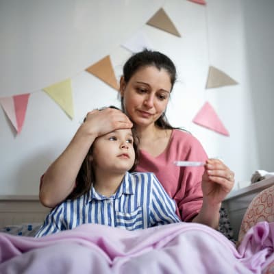 Mutter hält die Hand an die Stirn des Kindes und ein Thermometer in der anderen Hand